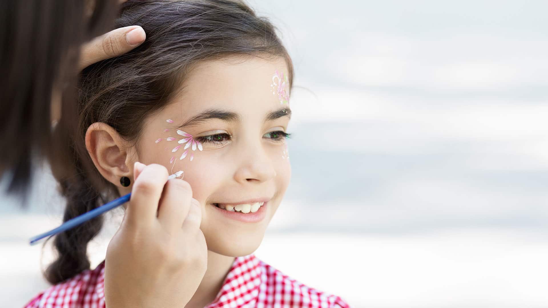 Cute happy girl getting floral face painting outdoors, copy space